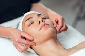 Cosmetologist making face massage for rejuvenation to woman while lying on a stretcher in the spa center.