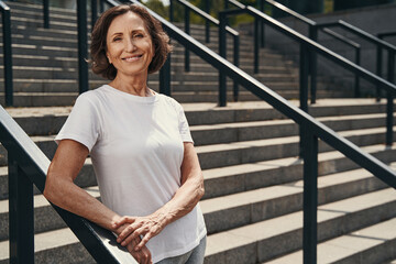 Joyful slim elderly woman standing on open stairs