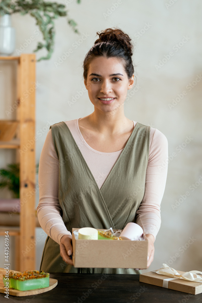 Wall mural Young cheerful female in smart casualwear holding cardboard giftbox with present