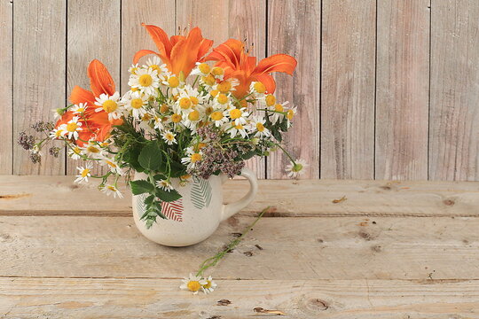 Chamomiles and lilies in a mug on an old wooden table, Abstract flower arrangement, background, minimal holiday concept, rustic style. Mother's day card, happy birthday, wedding, place for text