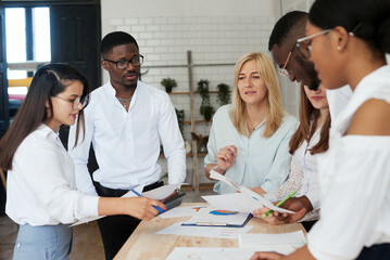 A team of multiethnic people are discussing business in the office. The employees of the company communicate, looking at the schedules and discussing the further strategy