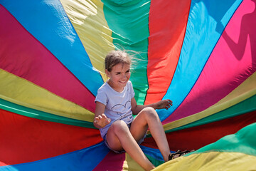 Happy girl having fun and waving in the center of bright colorful parachute, outdoors party, summer...