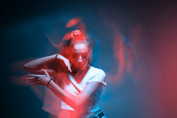 Mixed race young modern girl dancing in colourful neon light. Long exposure. Stylish female moving...