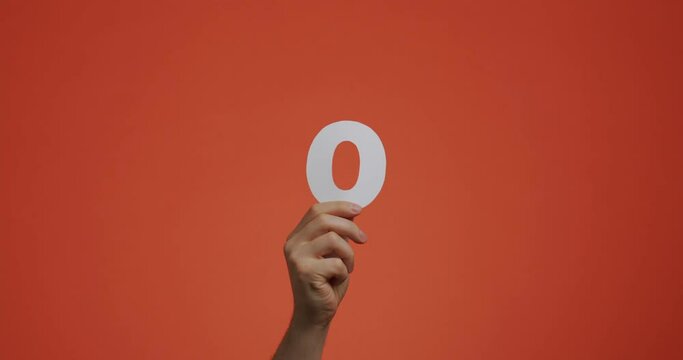 Number zero in hand. Arm showing digits, null numeral made of carved paper for voting or learning