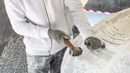 Detail of artist's hands sculpting marble with hammer and chisel