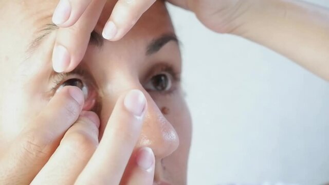 Close-up of a woman wearing soft contact lenses over her eyes against a white background. Myopia.