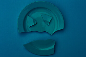 Blue broken plate on a blue background. Family relationship concept, divorce, horror.
