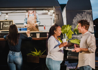 Diverse friends with food and drink speaking in park in evening