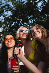 Low angle view of smiling multiethnic women with plastic cup holding microphone outdoors during party
