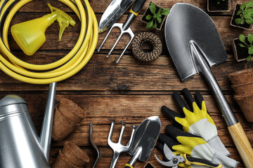 Frame of gardening tools and green plants on wooden background, flat lay