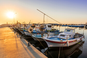 Fototapeta premium tranquil sunrise in fishing docks with sunny pier , leading far to sea and golden sun with sailing boats moored around