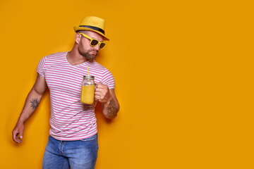 Creative male in sunglasses and summer clothes, stylish hat standing relaxed and drinking from...