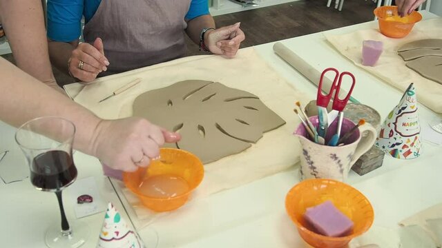 Woman hand potter making clay monstera leaf in pottery workshop studio. Process of creating ceramic vase. Handmade, hobby art and handicraft concept.