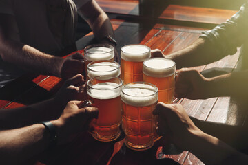 Friends clinking glasses with beer at table, closeup