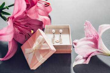 Set of pearl jewellery in pink gift box with flowers. Earrings and ring with lily on grey background