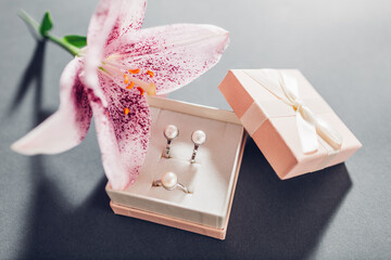 Set of pearl jewellery in pink gift box with flowers. Earrings and ring with lily on grey background