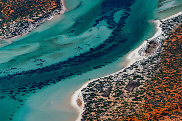 Abstract aerial view of blue-green water in shifting red deposition of sediment gradually moving through alluvial plains of Francois Peron National Park in Western Australia.