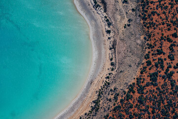Abstract aerial view of blue-green water in shifting red deposition of sediment gradually moving through alluvial plains of Francois Peron National Park in Western Australia.