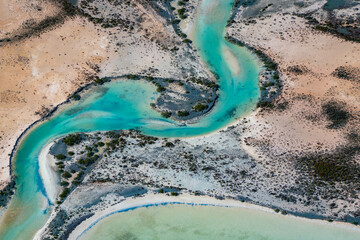 Abstract aerial view of blue-green water in shifting red deposition of sediment gradually moving through alluvial plains of Francois Peron National Park in Western Australia.