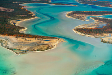 Abstract aerial view of blue-green water in shifting red deposition of sediment gradually moving through alluvial plains of Francois Peron National Park in Western Australia.