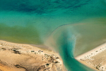 Abstract aerial view of blue-green water in shifting red deposition of sediment gradually moving through alluvial plains of Francois Peron National Park in Western Australia.