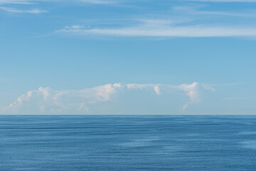 Blue, little cloudy sky over the calm Pacific Ocean.