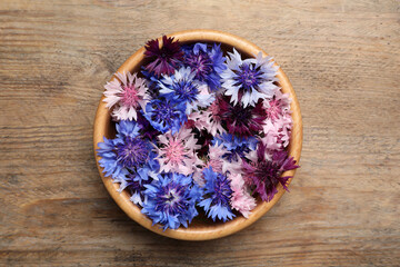 Obraz na płótnie Canvas Beautiful colorful cornflowers in bowl on wooden table, top view