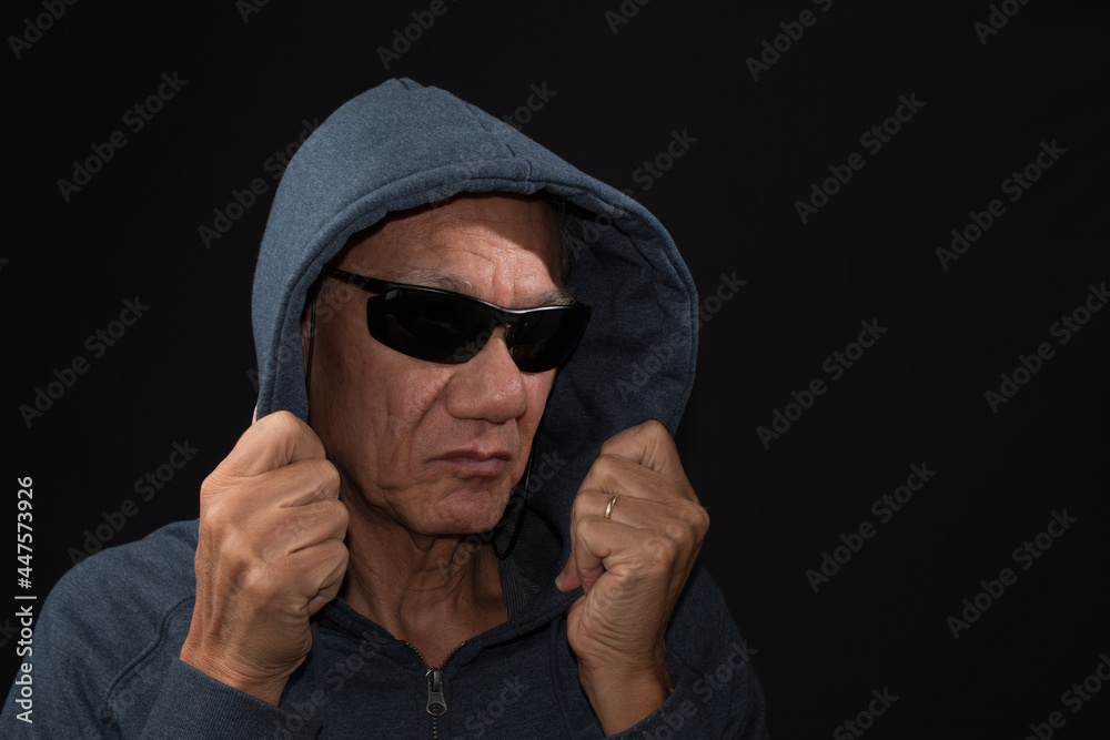 Wall mural Older man wearing a dark hoodie and shades against a black background