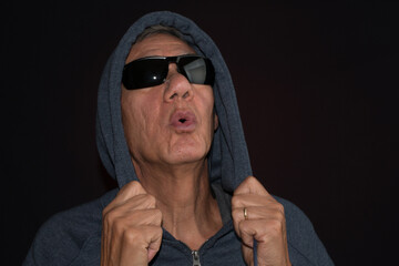 Older man wearing a dark hoodie and shades against a black background