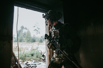 Military man with assault rifle standing inside building, he is ready for combat