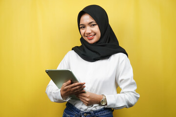 Beautiful young asian muslim woman smiling, excited and cheerful holding tablet, isolated on yellow background