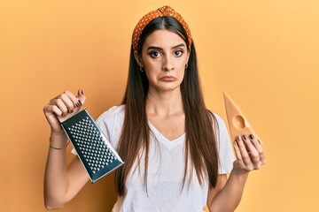 Beautiful brunette young woman holding grater and cheese depressed and worry for distress, crying...