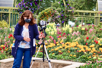 Fototapeta na wymiar Woman Photographer Taking Pictures of Flowers Wearing a Mask During Covid