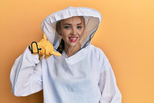 Beautiful Blonde Caucasian Woman Wearing Protective Beekeeper Uniform Smiling Doing Phone Gesture With Hand And Fingers Like Talking On The Telephone. Communicating Concepts.