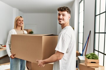 Fototapeta na wymiar Young caucasian couple smiling happy holding cardboard boxes standing at new home.