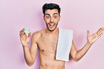 Young hispanic man shirtless wearing towel and eye bags patches celebrating victory with happy smile and winner expression with raised hands