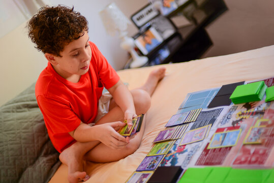 boy playing with yugioh's cards, boy in room playing cards alone, child playing at home, boy playing at home, playing in the room, sitting on the bed, Children's Day, focused