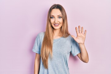 Young blonde girl wearing casual t shirt showing and pointing up with fingers number five while smiling confident and happy.