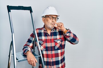 Handsome mature handyman close to construction stairs wearing hardhat mouth and lips shut as zip...