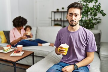 Hispanic father of interracial family drinking a cup coffee depressed and worry for distress, crying angry and afraid. sad expression.