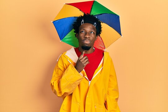 Young african american man wearing yellow raincoat thinking concentrated about doubt with finger on chin and looking up wondering