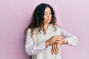 Young brunette woman with curly hair wearing casual clothes checking the time on wrist watch, relaxed and confident