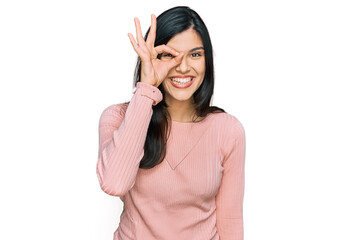 Young hispanic woman wearing casual clothes doing ok gesture with hand smiling, eye looking through fingers with happy face.