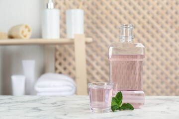 Fototapeta na wymiar Bottle and glass with mouthwash on white marble table in bathroom, space for text