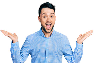 Fototapeta premium Hispanic man with beard wearing casual business shirt celebrating crazy and amazed for success with arms raised and open eyes screaming excited. winner concept