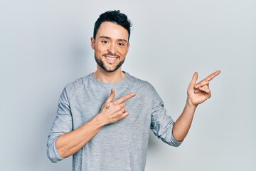 Young hispanic man pointing with fingers to the side smiling with a happy and cool smile on face. showing teeth.