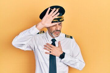 Handsome middle age man with grey hair wearing airplane pilot uniform touching forehead for illness and fever, flu and cold, virus sick