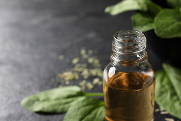 Essential oil of broadleaf plantain on black table, closeup. Space for text