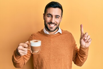 Young hispanic man holding coffee smiling with an idea or question pointing finger with happy face, number one