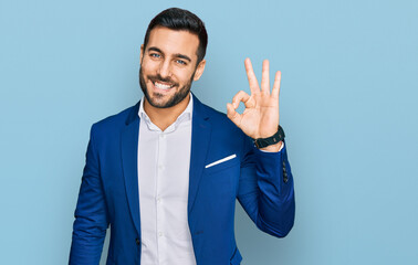 Young hispanic man wearing business jacket smiling positive doing ok sign with hand and fingers. successful expression.